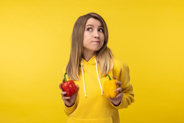 La photo d'une jolie femme tient des papiers et semble curieuse de quelque chose. Porte un sweat à capuche jaune décontracté, fond de couleur jaune isolé.