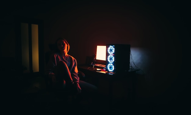 photo d'une jolie fille assise sur une chaise près d'un ordinateur au feu rouge Travail de nuit sur l'ordinateur