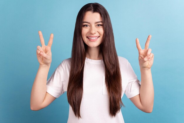 Photo d'une jolie fille gaie montrant les doigts de la paix cool v-symbol bonne humeur isolée sur fond de couleur bleue.