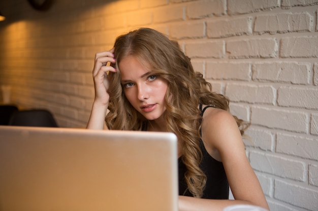 Photo de jolie fille yong aux cheveux bouclés assis dans un café travaillant par son ordinateur portable