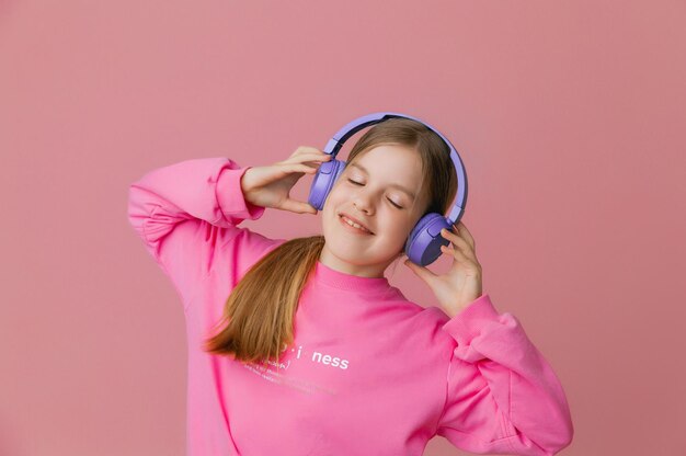 Photo d'une jolie jeune adolescente drôle dans un casque de cavalier rose dansant en écoutant de la musique sur un fond