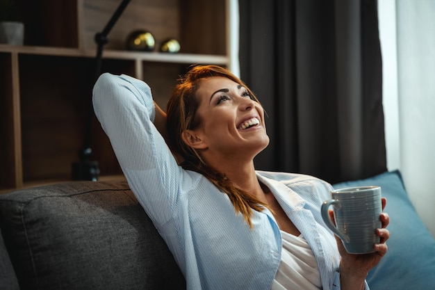 Photo d'une jolie jeune femme assise sur le canapé et dégustant une tasse de café à la maison.