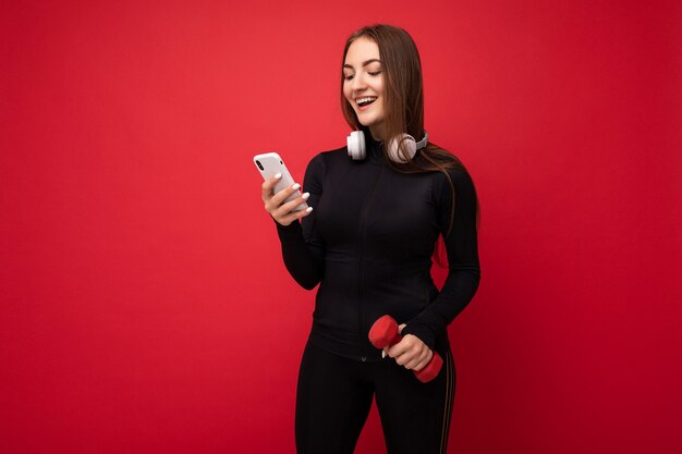 Photo d'une jolie jeune femme brune positive souriante portant des vêtements de sport noirs blancs