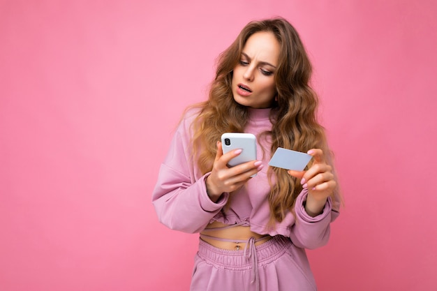 Photo de jolie jeune femme frisée blonde en colère demandant des vêtements roses isolés sur rose