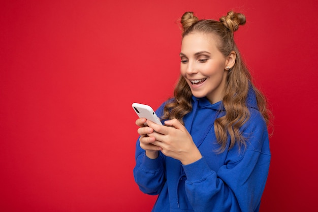 Photo d'une jolie jeune femme positive et séduisante portant une tenue élégante décontractée isolée sur fond avec un espace vide tenant dans la main et utilisant des sms de messagerie pour téléphone portable en regardant