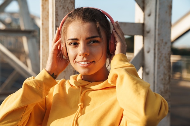 Photo d'une jolie jeune femme de remise en forme optimiste et positive posant à l'extérieur en écoutant de la musique avec des écouteurs.