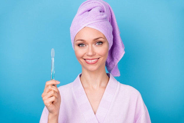 Photo d'une jolie jeune femme tenir une brosse à dents regarder l'appareil photo porter une serviette violette turban peignoir isolé sur fond de couleur bleu