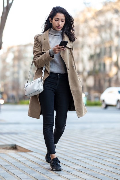 Photo d'une jolie jeune femme utilisant son smartphone en marchant dans la rue.