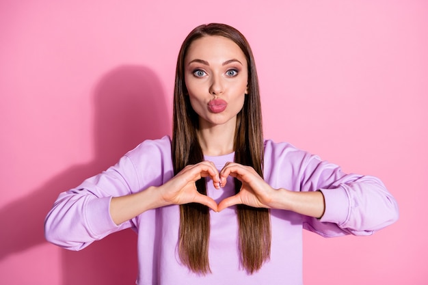 Photo de jolies mains de dame attrayantes les bras montrent le symbole du coeur expriment des sentiments cardiaques rendez-vous romantique envoyer des baisers aériens petit ami porter un pull violet décontracté isolé fond de couleur pastel rose