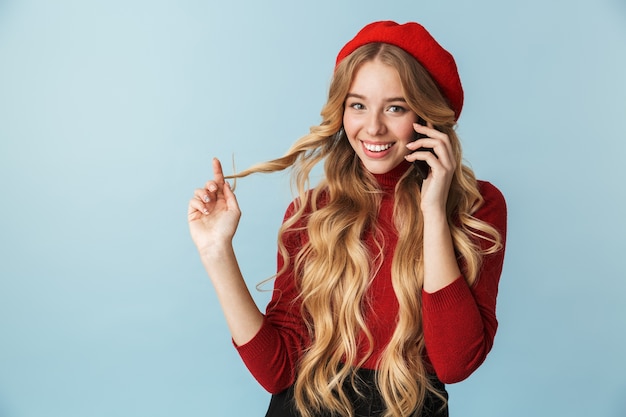 Photo de joyeuse jeune fille de 20 ans portant un béret rouge parlant au téléphone portable isolé