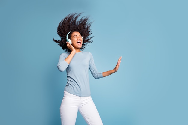 Photo de joyeuse positive mignonne jolie jolie petite amie inspirée de son groupe de rock préféré en pantalon blanc pull bleu près de l'espace vide chantant avec des cheveux soufflés fond de couleur pastel isolé