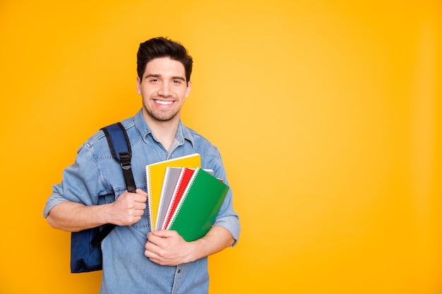 Photo de joyeux homme positif près de l'espace vide tenant des blocs-notes colorés avec sac à dos derrière mur de couleur vive isolé