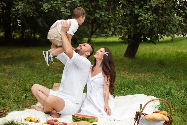 Photo de joyeux jeune femme et homme caucasien tient leur enfant sur les mains, sourit et se réjouit