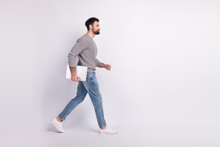 Photo latérale du profil complet du corps d'un jeune homme à pied tenir un représentant d'ordinateur portable isolé sur fond de couleur grise