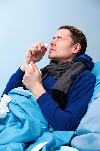 Photo latérale d'un homme brun malade utilisant un spray nasal en position couchée dans son lit