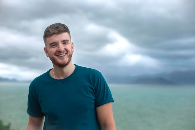 Photo latérale de profil d'un beau mec heureux jeune homme appréciant le paysage de vue sur l'océan de la mer regardant à distance le jour d'été dans un pays tropical à la tempête avec un ciel nuageux respirant de l'air frais profond