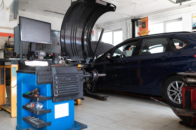 Photo d'une machine pour équilibrer les roues et réparer les pneus d'une voiture dans le contexte d'une voiture de tourisme bleue dans une station-service lors d'une réparation avec un capot ouvert