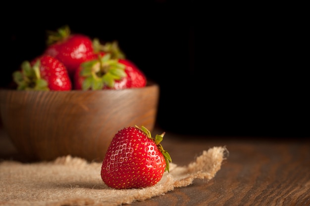 Photo macro de fraise rouge mûre fraîche dans un bol en bois sur fond rustique. Produits naturels biologiques.