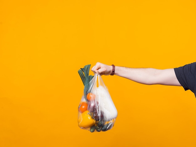 Photo d'une main d'homme tenant une pochette d'épicerie près d'un mur jaune