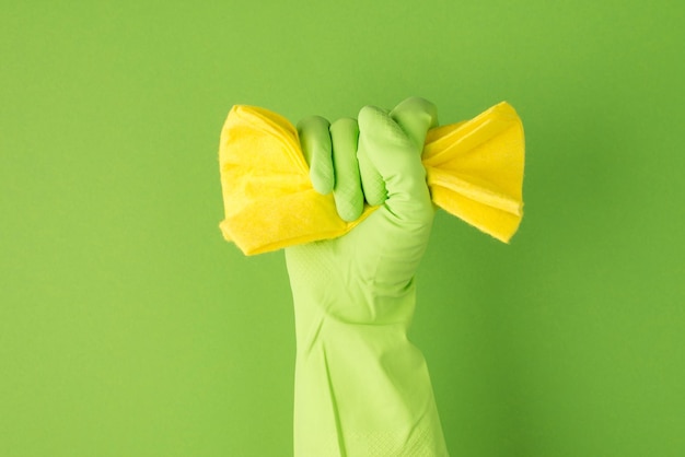 Photo de main levée dans un gant en caoutchouc vert serrant une serviette jaune sur fond vert isolé avec espace pour copie