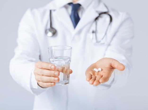 photo de mains de docteur donnant des pilules blanches et un verre d'eau