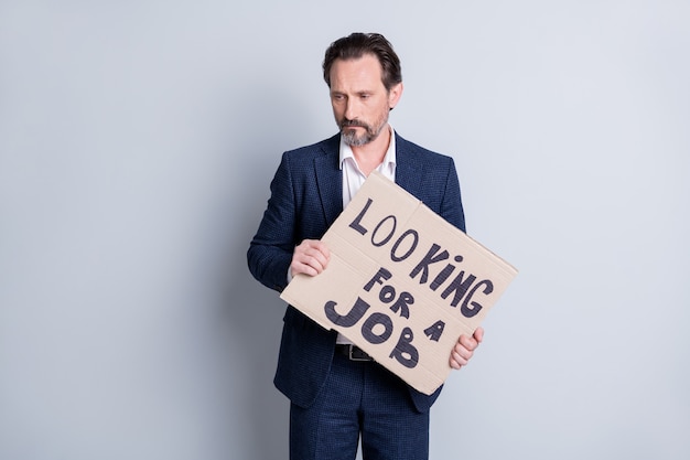 Photo de malheureux triste travailleur stressé âgé d'âge mûr perdant homme d'affaires crise financière emploi perdu tenir carton placard recherche travail demander de l'aide marché du travail porter costume isolé fond gris