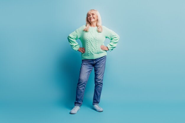 Photo de mamie joyeuse mettre les mains sur la taille sur fond bleu pastel