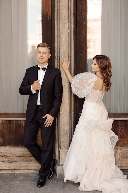 Photo des mariés qui se parlent et se regardent sur fond de portes. Entrée du bâtiment. Robe de mariée, costume. Notion de jour de mariage. photo de haute qualité