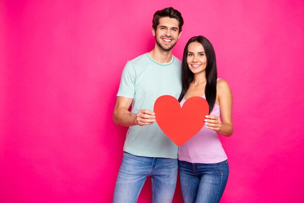 Photo de mec étonnant et dame étreignant tenant grand coeur de papier dans les mains exprimant une attitude positive usure tenue décontractée fond de couleur rose isolé