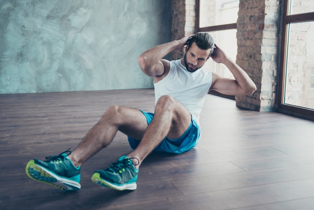 Photo de mec sportif macho faisant des redressements assis statique sol personne déterminée sportswear débardeur shorts baskets formation maison windows à l'intérieur