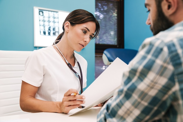 Photo d'un médecin sérieux concentré parlant avec un patient à l'hôpital à la table.