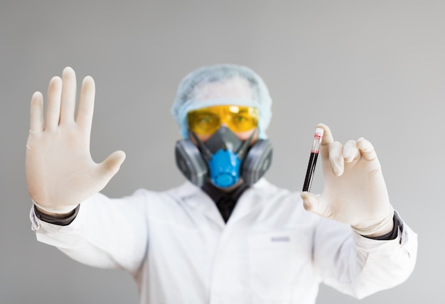 Photo d'un médecin en tenue de protection tenant un tube à essai avec un échantillon de sang infecté dans son ha...