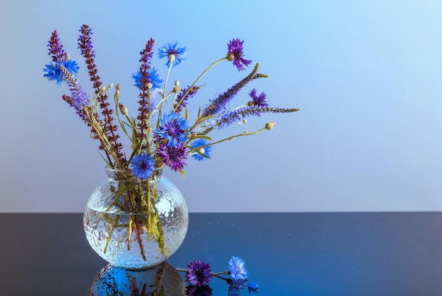 Photo minimaliste de fleurs de bleuet bleu et violet avec des herbes sauvages en bouquet sur table sur fond bleu