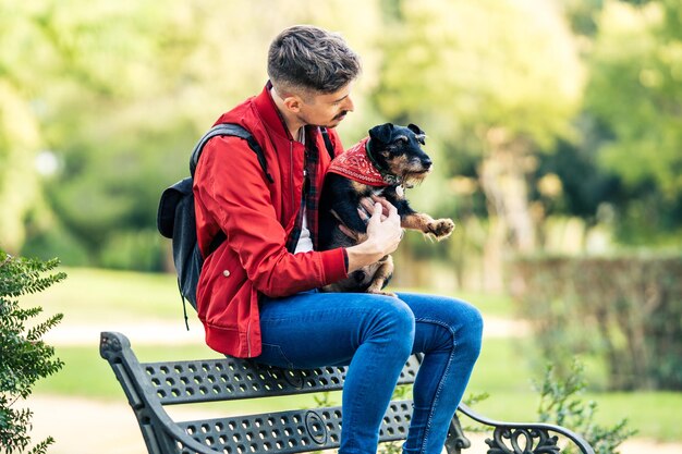 Photo avec mise au point sélective sur un homme embrassant un petit chien assis sur un banc dans un parc public