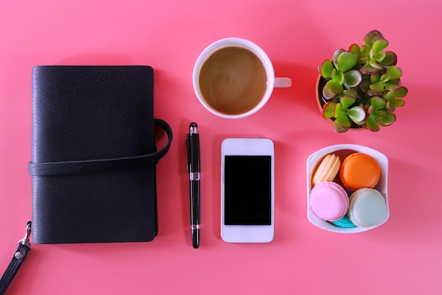 photo de mise à plat avec bloc-notes, smartphone, tasse à café, macaron et plante tropicale