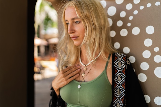 Photo de mode de belle femme blonde en tenue d'été bohème posant à l'extérieur portant un collier élégant Ambiance tropicale