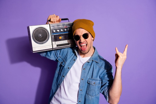 Photo de mode élégant homme criant blanc tenant un enregistreur rétro avec les mains vous montrant signe de roche criant portant des chapeaux de casquette t-shirt en denim isolé fond de couleur vive violet