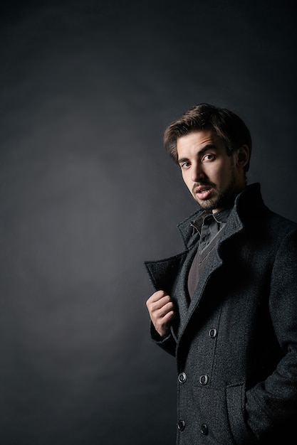 Photo de mode d'un jeune bel homme en manteau sur fond noir