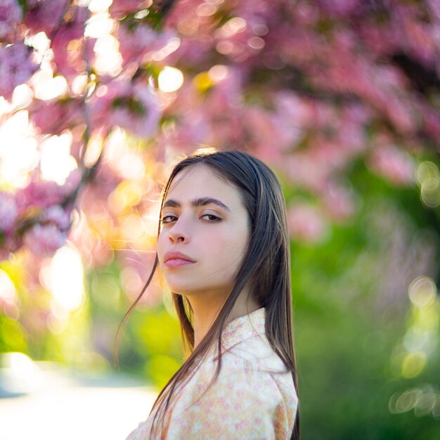 Photo de mode en plein air d'une belle jeune femme entourée de fleurs printemps fleur de cerisier