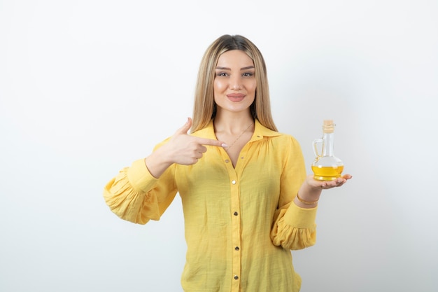 Photo d'un modèle de belle femme en chemise jaune pointant sur une bouteille en verre d'huile