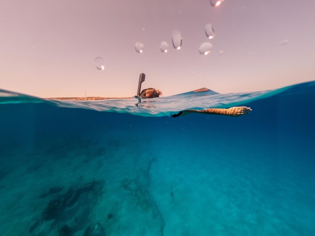Photo à moitié sous-marine d'une femme faisant de la plongée avec tuba dans une eau cristalline