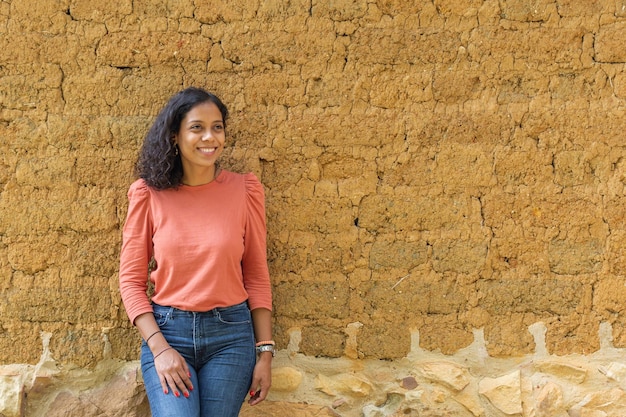 Photo moyenne d'une belle femme hispanique regardant sur le côté souriante et posant détendue avec un mur d'adobe en arrière-plan