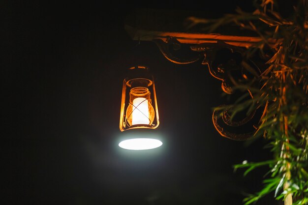 Photo nocturne en plein air d'une lanterne antique accrochée à un poteau en bois dans le jardin