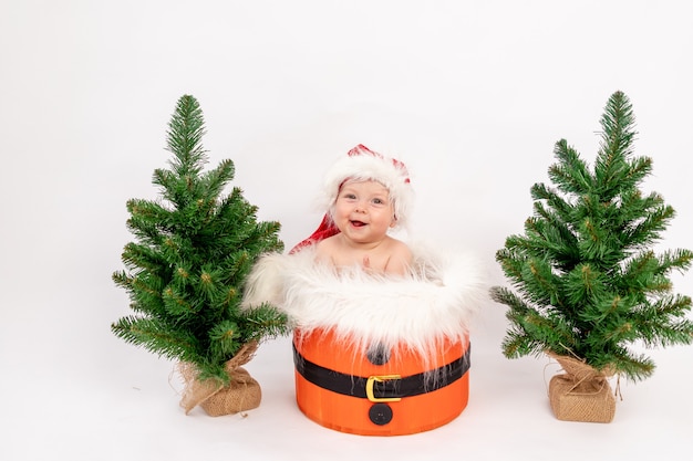 Photo de Noël une petite fille enfant assise dans un bonnet de Noel dans un panier près des arbres de Noël