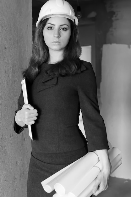 Photo en noir et blanc d'une femme architecte sur le chantier avec dessins et cahier