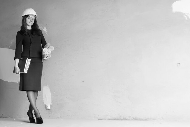 Photo en noir et blanc d'une femme architecte sur le chantier avec dessins et cahier