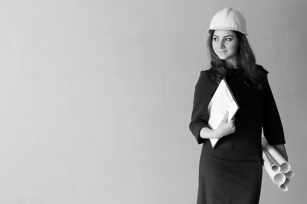 Photo en noir et blanc d'une femme architecte sur le chantier avec dessins et cahier