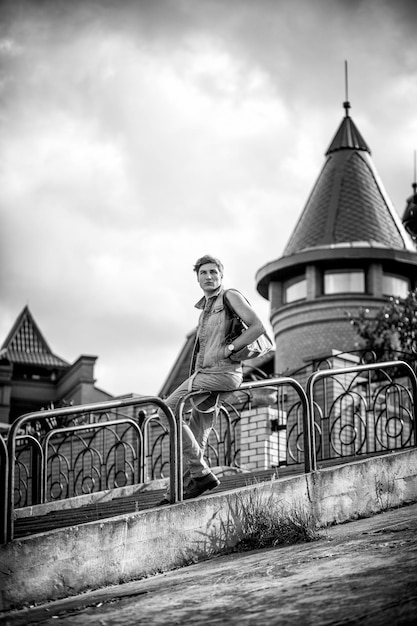 Photo en noir et blanc d'un gars de la mode avec un sac assis sur les rails