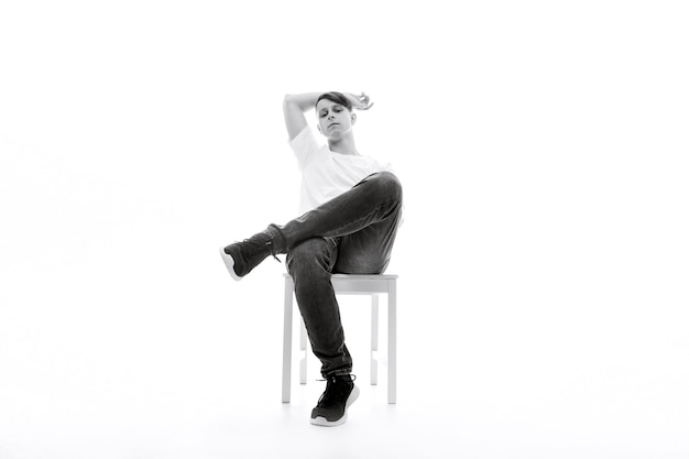 Photo en noir et blanc d'un homme assis sur une chaise blanche sur un fond blanc jambes croisées