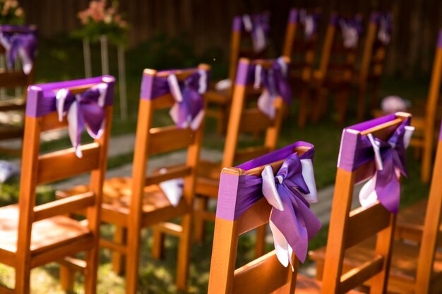 Photo sur la photo, nous voyons des chaises décorées de rubans lavande lilas. cérémonie de mariage en plein air